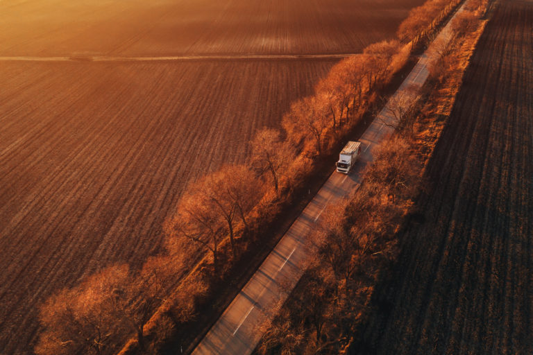 Aerial view of semi-truck on the road in sunset, drone pov of vehicle in rural countryside landscape